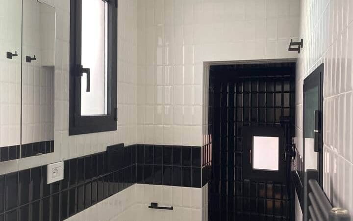 Second bathroom tiled in white and black brick tiles, with a basin, a mirrored cabinet, a heated towel rail and a walk-in shower behind a black-tiled wall