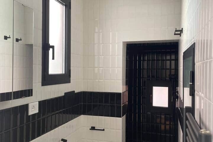 Second bathroom tiled in white and black brick tiles, with a basin, a mirrored cabinet, a heated towel rail and a walk-in shower behind a black-tiled wall