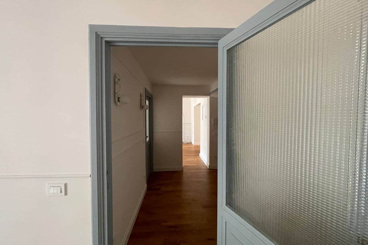 Hallway with dark oak floorboards running towards a lit room, framed by a grey-green door glazed with reeded glass